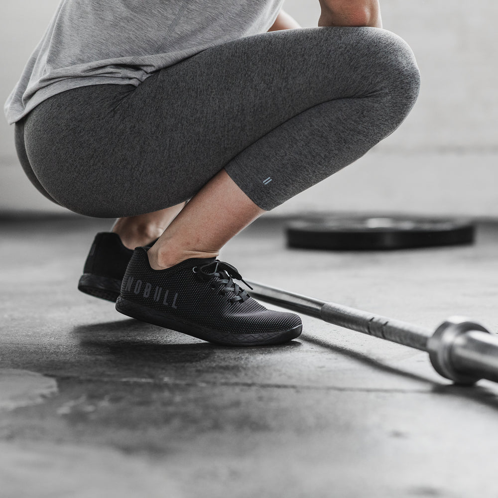 A woman wearing gray athletic clothing and black cross training shoes squats before her next workout set