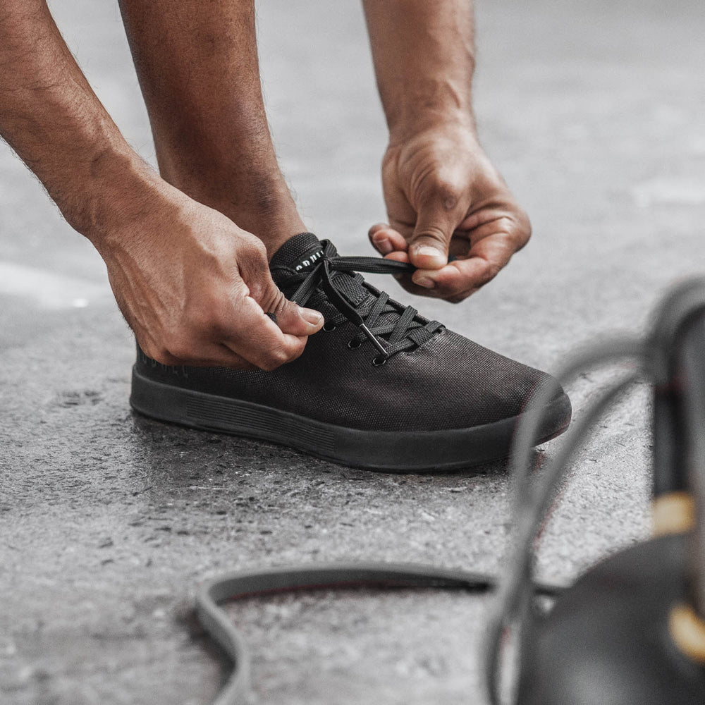 An athletic man is lacing up all black canvas training sneakers before his workout