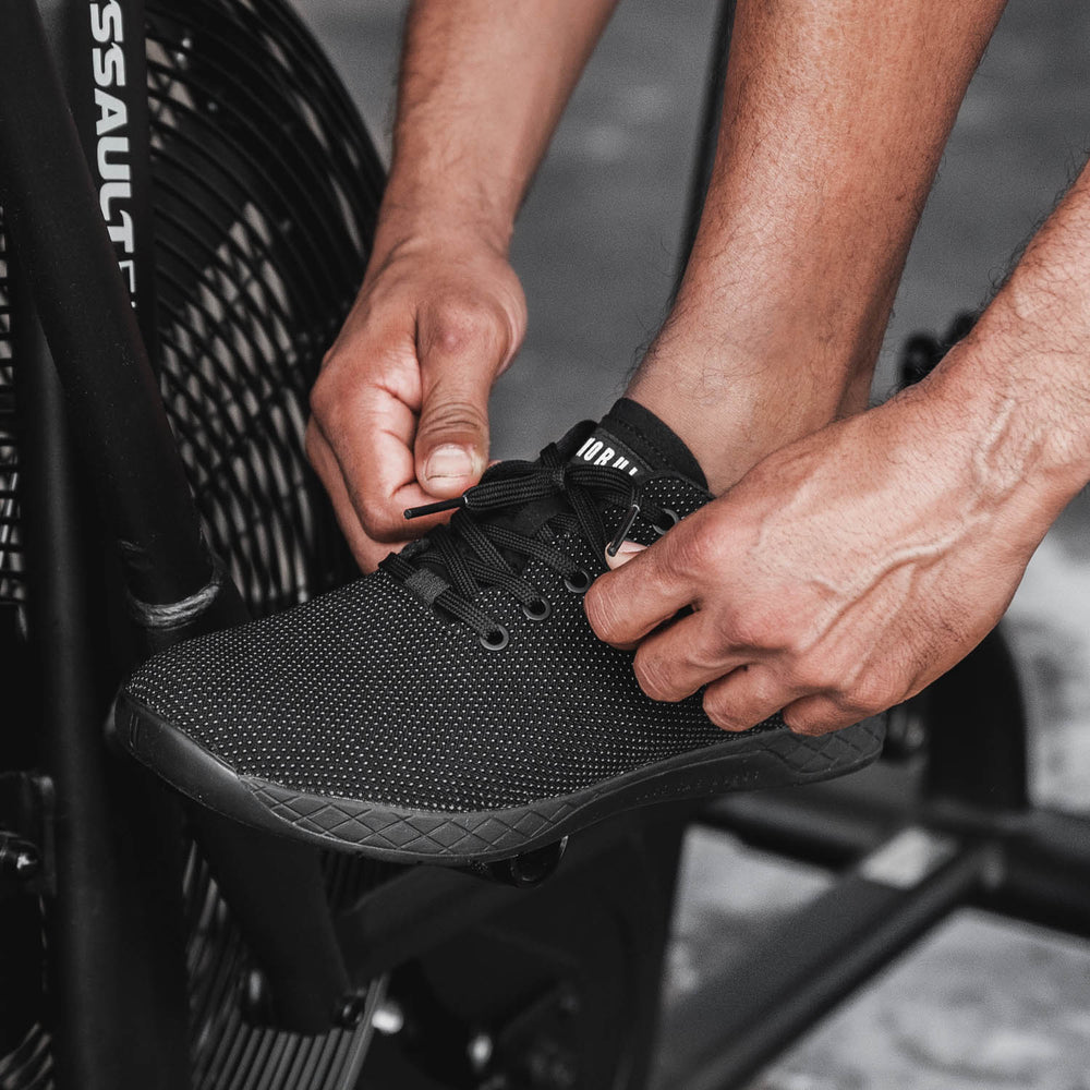 A man wearing all black trainer shoes is tying his shoes before performing a cycling workout