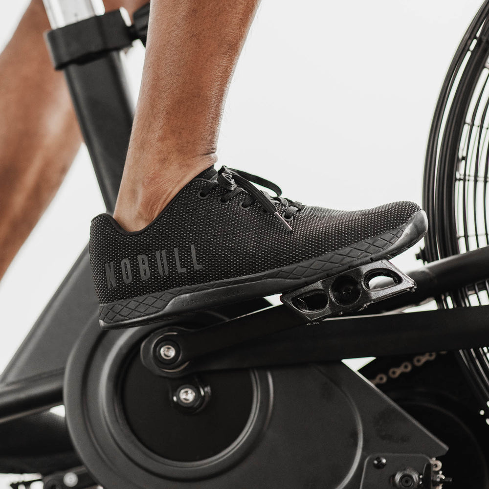 A man wearing all black trainer shoes is performing a cycling workout