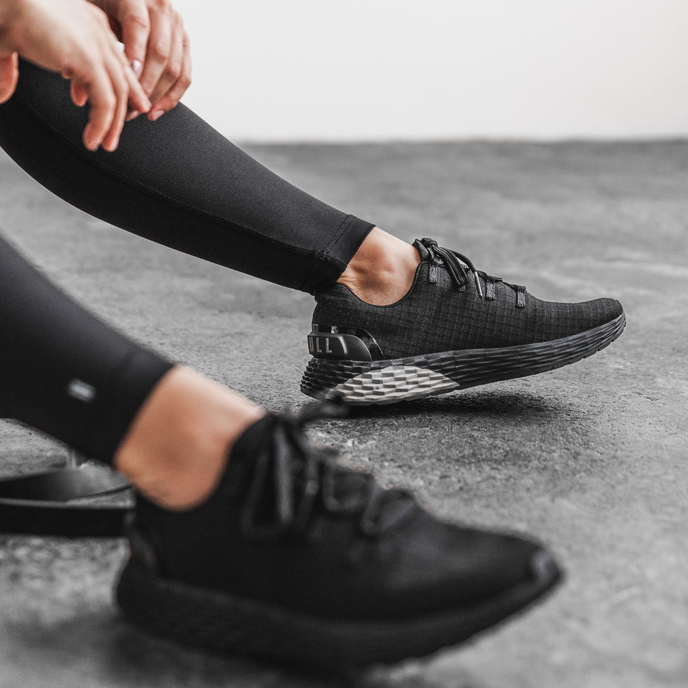 A woman resting between sets wearing all black ripstop runner training sneakers