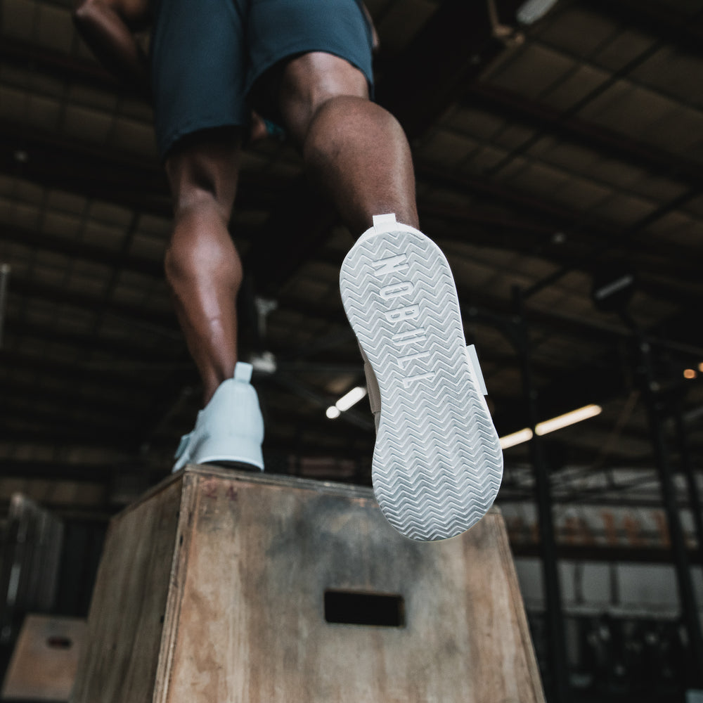 An athletic man wearing casual workout apparel and Arctic print canvas lifters performs box jumps