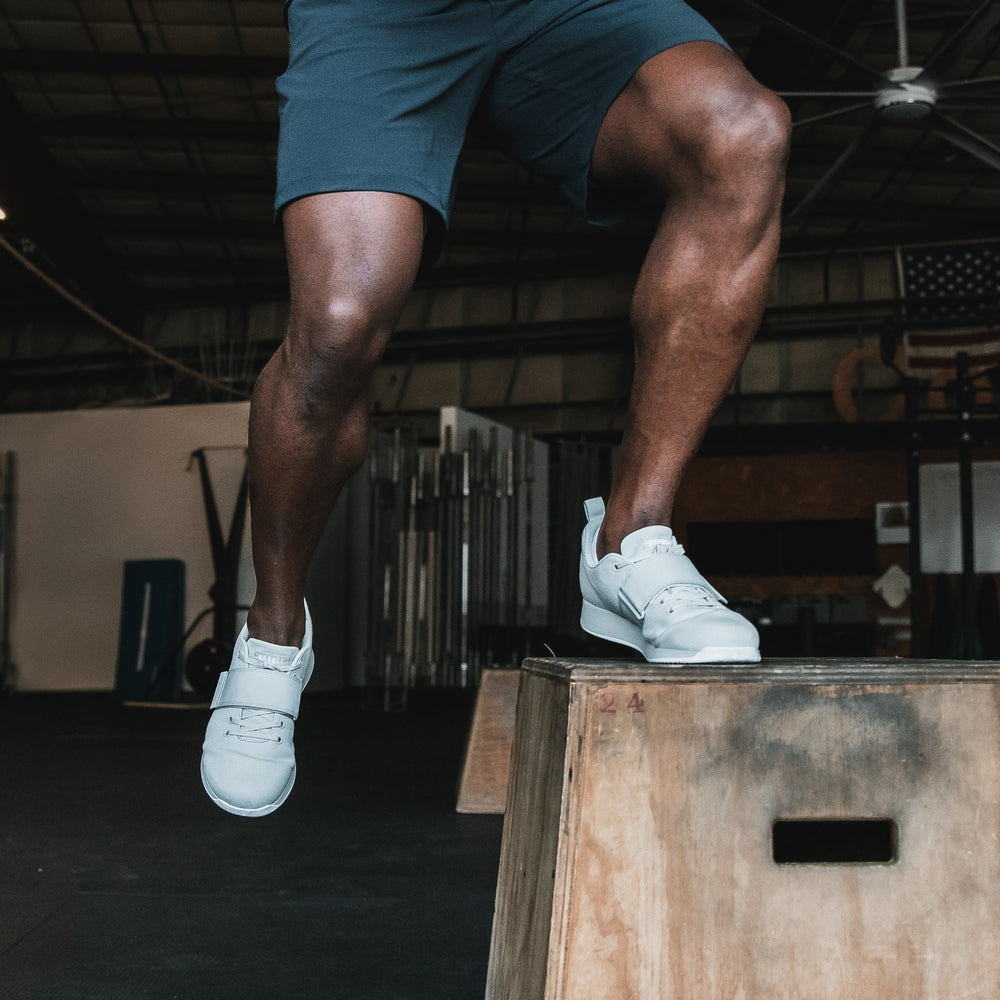 An athletic man is performing box jumps while wearing Arctic colored Canvas Lifter training shoes