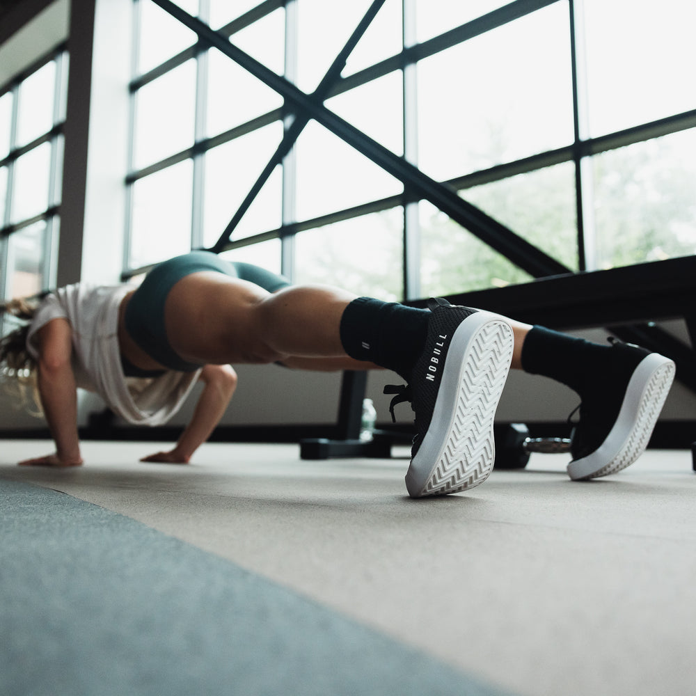 Athletic woman does pushups in athletic clothing while wearing black and white rec trainers