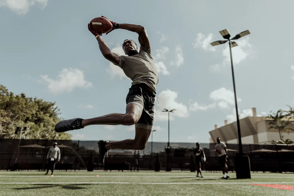 Athlete wearing athletic training clothes and cleats catches a football at the NFL Combine training