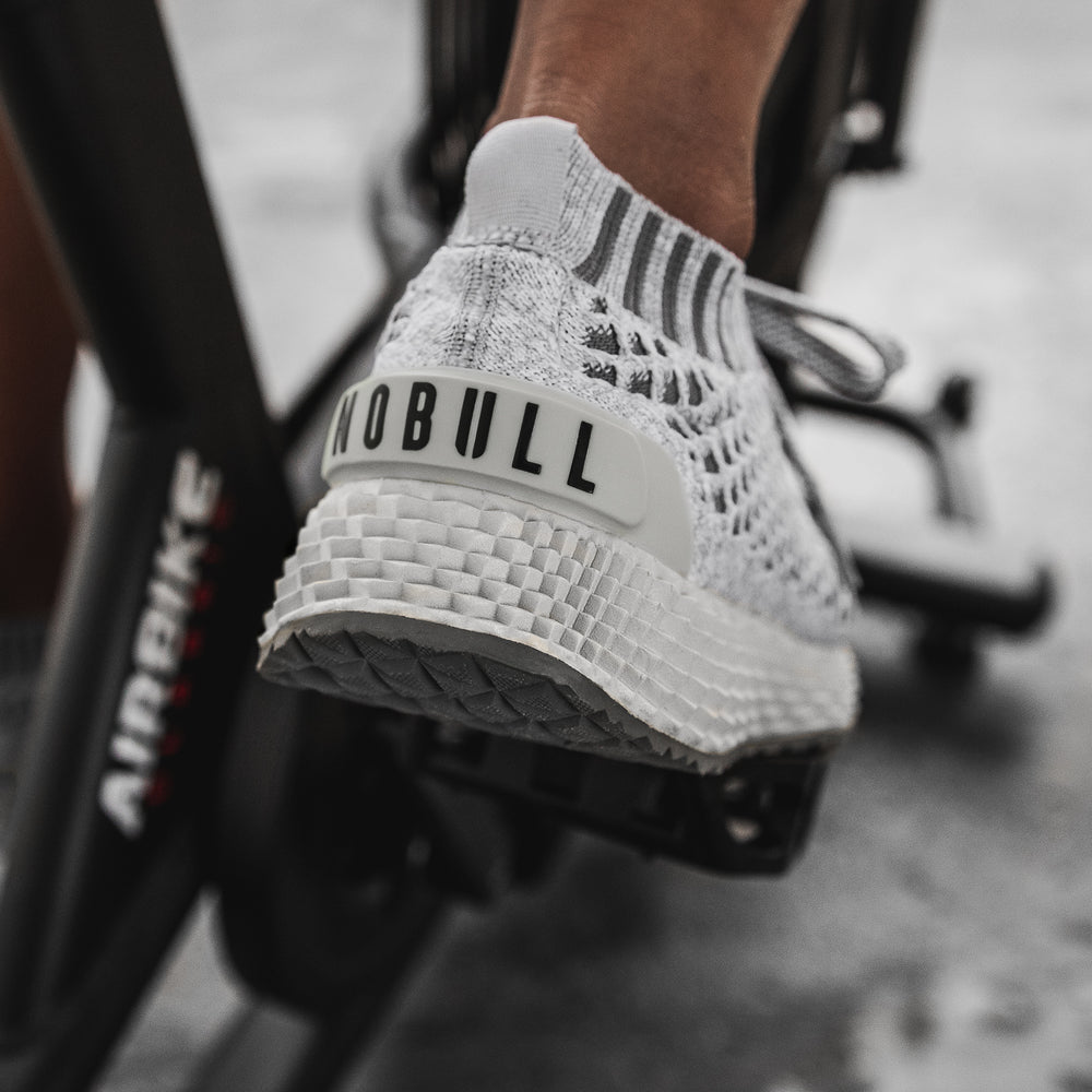 An athlete wearing light gray knit training shoes works out on a cycling bike