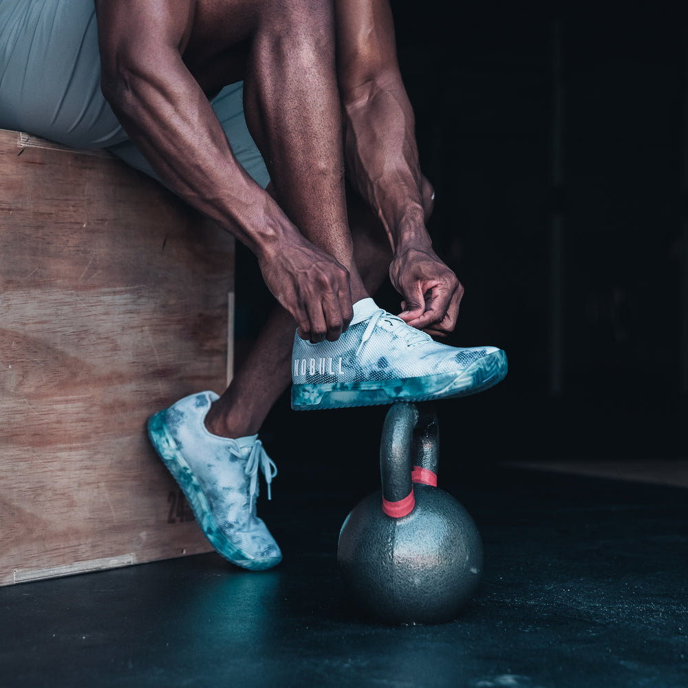 Athlete ties Mint colored tie-dye rec trainer shoes before a workout with a kettlebell