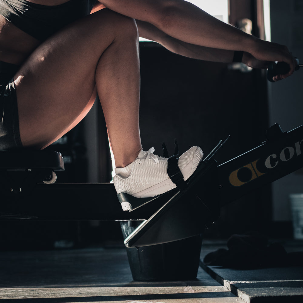 A woman wearing athletic apparel and white trainer plus cross training shoes performs a rowing workout