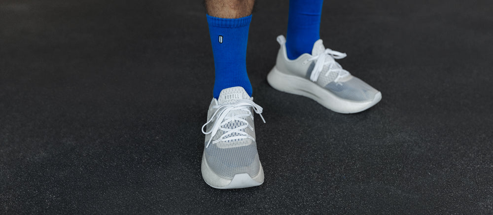An athlete wearing bright blue athletic socks and white translucent runner plus shoes